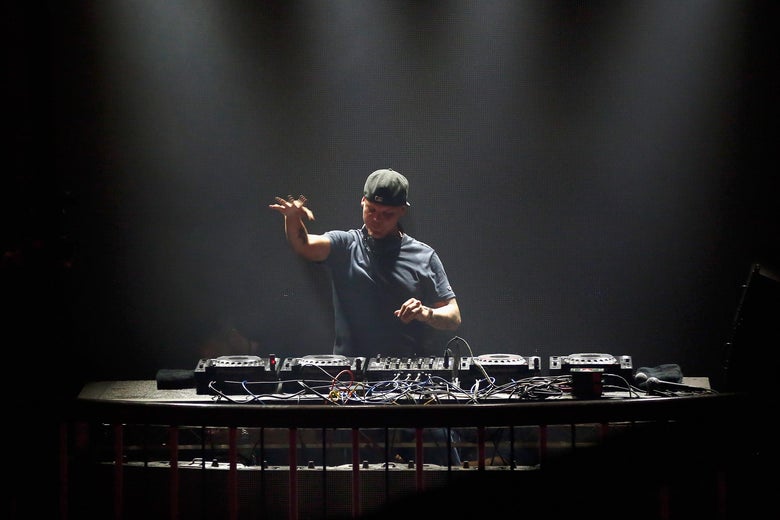 Avicii stands behind a turntable.